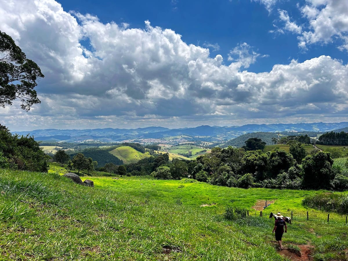 Vale verde visto do Alto das Pitangueiras, com afloramento rochoso em primeiro plano e montanhas da Mantiqueira ao fundo